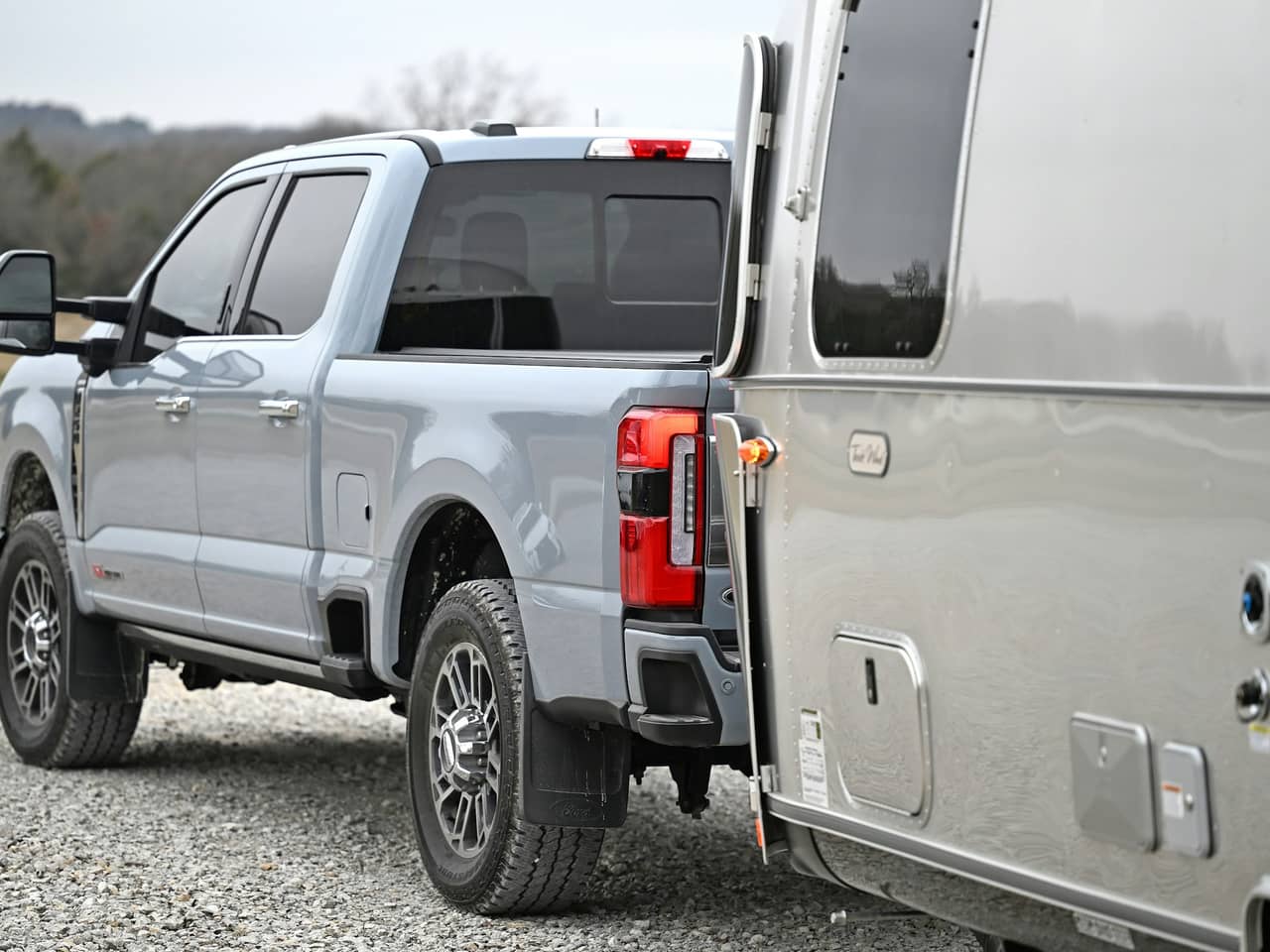 Light gray pickup hitched to a silver travel trailer on gravel