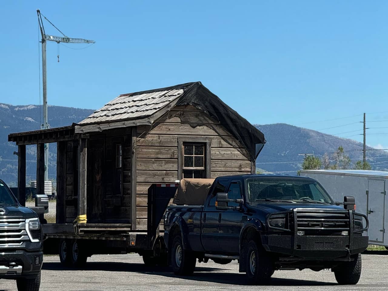 Dark pickup towing a small wooden cabin on a flatbed trailer
