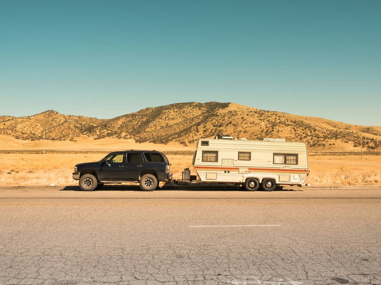 Dark SUV towing a white travel trailer on a desert road