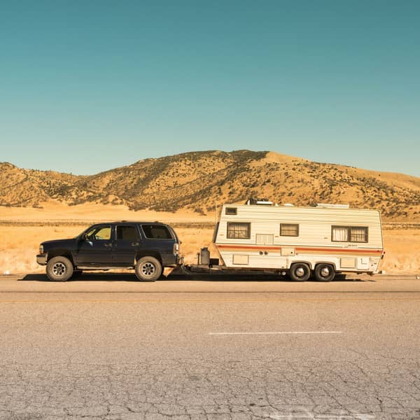Dark SUV towing a white travel trailer on a desert road