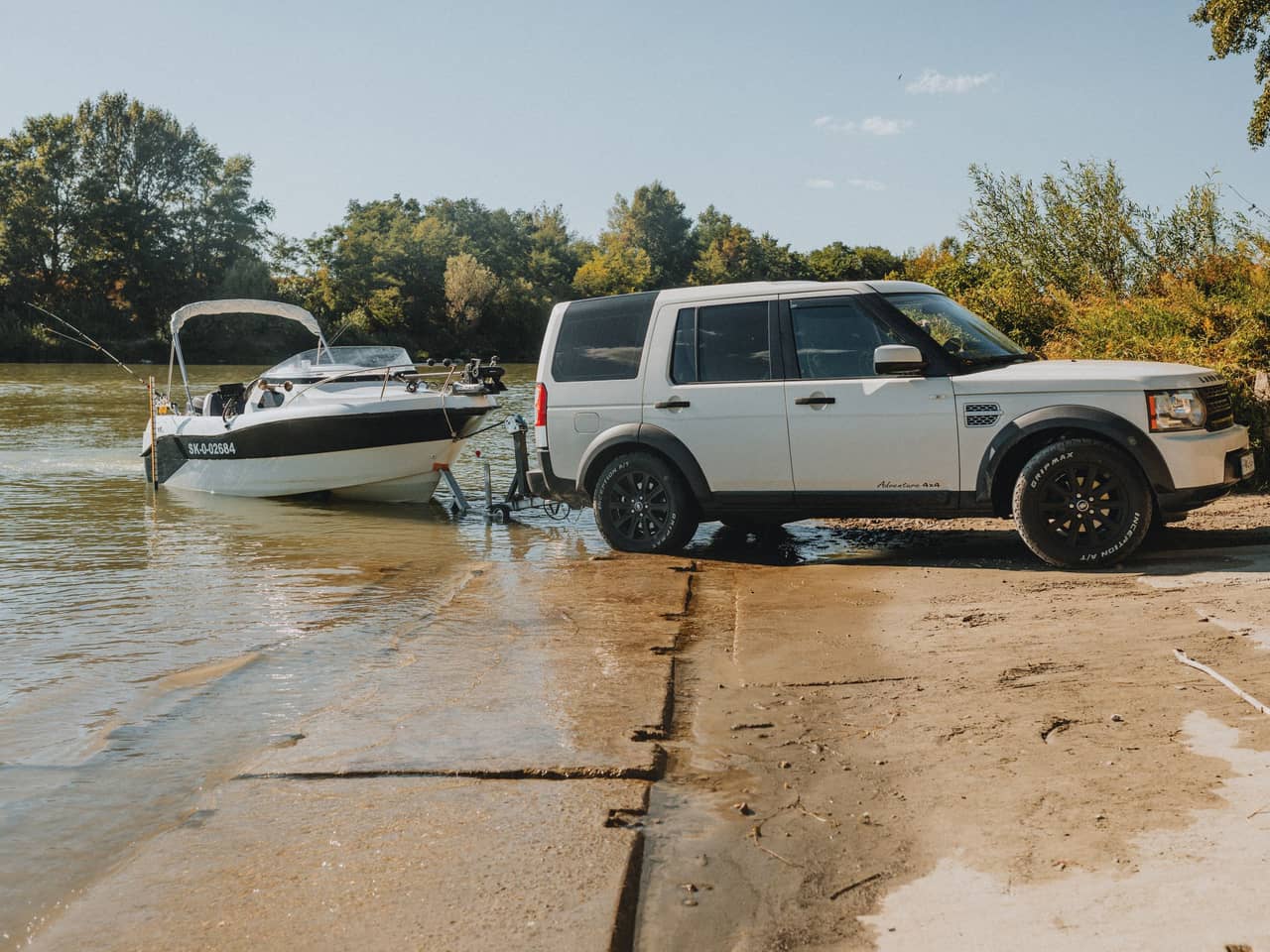 White SUV backing a boat trailer down a sandy launch ramp