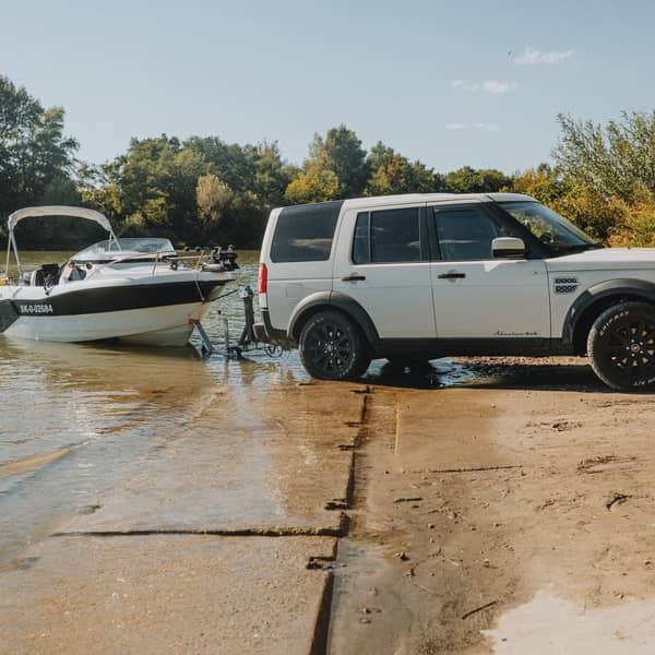White SUV backing a boat trailer down a sandy launch ramp